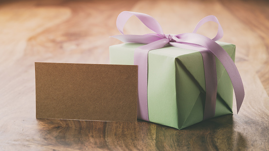 green gift box with purple ribbon bow on old wood table with greeting card, vintage toned