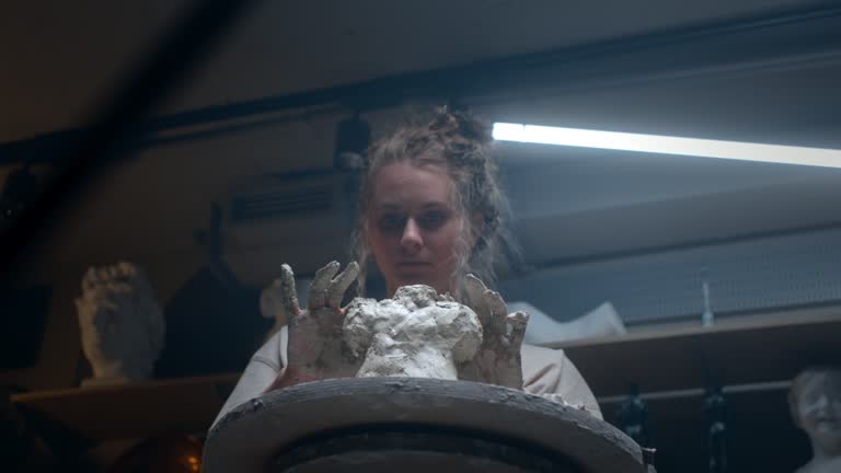 A talented sculptor girl creates a sculpture of a fat woman from clay with her hands. The female strikes with her fingers clay on an figure.