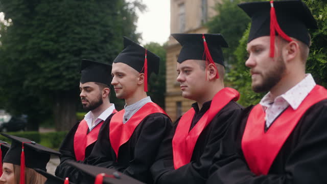 Students celebrate graduation. Young men dressed in gowns and graduation caps lined up for a photograph.