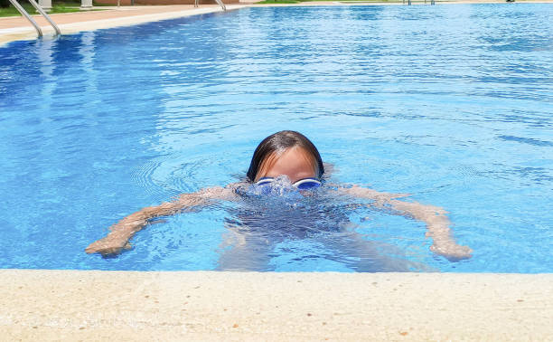 кавказская девочка, 7 лет, плавает в открытом бассейне, барахтается в воде. летний солнечный день. - female 8 9 years child excitement стоковые фото и изображения