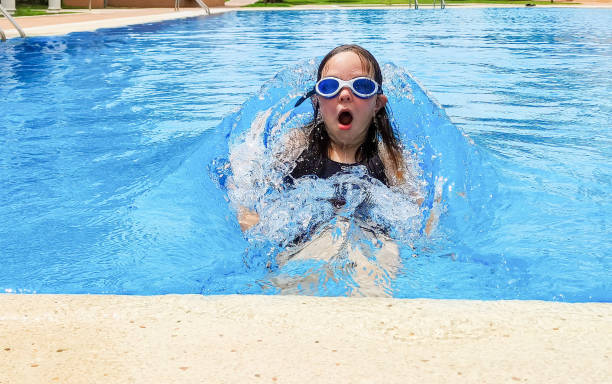 кавказская девочка, 7 лет, плавает �в открытом бассейне, барахтается в воде. летний солнечный день. - female 8 9 years child excitement стоковые фото и изображения