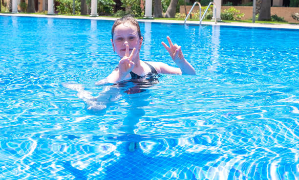 enfant fille de race blanche de 7 ans dans une piscine extérieure. gestures montre un symbole d’amour, un cœur. journée ensoleillée d’été. - female 8 9 years child excitement photos et images de collection