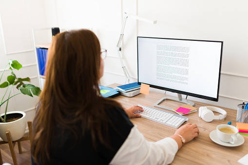 Professional big woman seen from behind working in her office and using her desk computer while looking at the screen