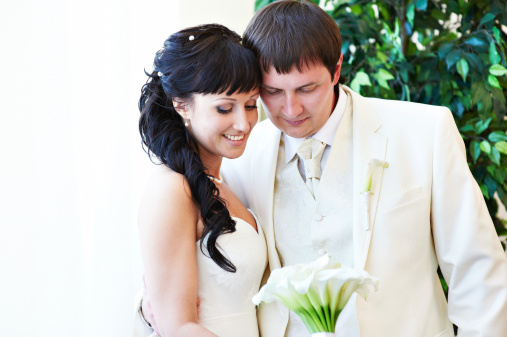 Happy bride and groom look at bouquet in wedding day