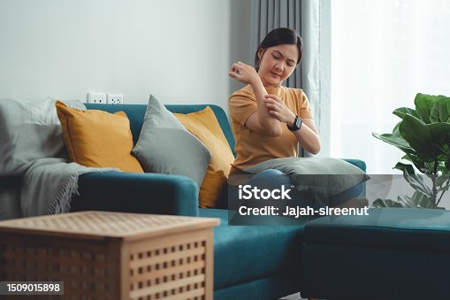 istock Asian woman irritate itching dry skin scratching her skin sitting on sofa in living room at home. 1509015898