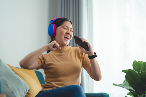 Happy woman using smartphone with headphones listening to music enjoy and dancing at home.
