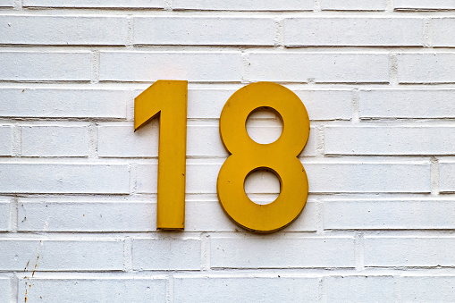 White brick wall with yellow sign on it that says'18 ' in Germany.