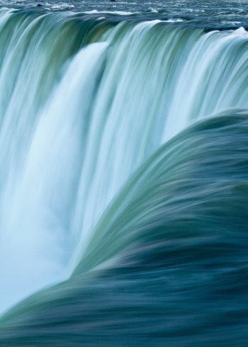 Close up of blue green water racing over the edge of Niagara Falls waterfall, Horseshoe Falls, Canada.