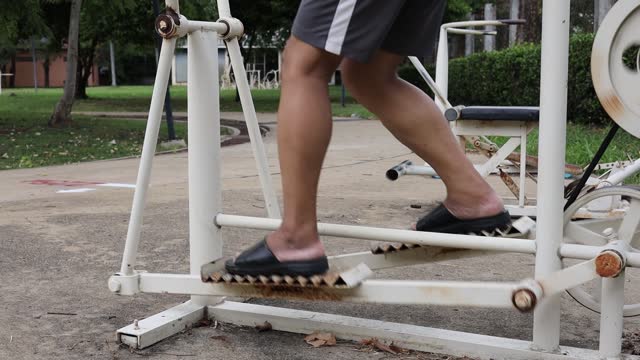 Close-up view of feet and legs of a Thai man exercising on an old white iron exercise bike.