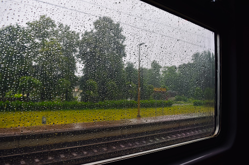 View from the train window on rainy weather in summer. The train window is covered in raindrops.