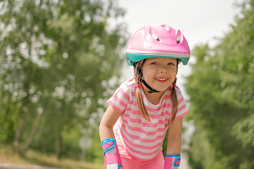 Laughing funny girl with pigtails in a striped T-shirt in a sports protective helmet looks at the camera while roller skating