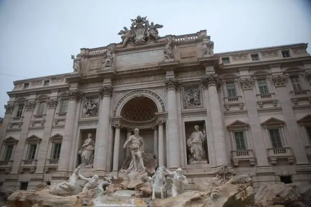 The large Trevi Fountain adorns the exterior of a modern building, its features illuminated by the sun