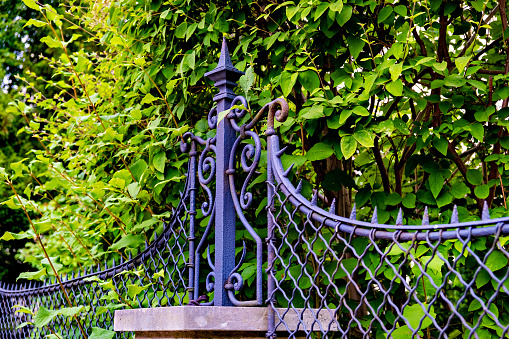 A brick post with a black iron fence and a green bush behind it in Germany.