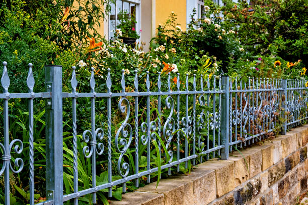 valla de metal azul con flores creciendo en ella y construyendo en el fondo en alemania. - formal garden front or back yard gazebo night fotografías e imágenes de stock