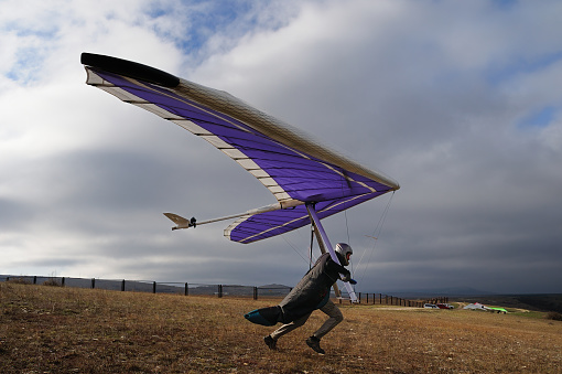 Hang glider pilot runs fast on a slope before being airborne. Extreme sport