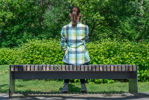 Woman sitting on park bench and talking on mobile phone. Young adult use smart phone for chatting. Female resting and conversation on the cell phone. Leisure, technology and modern lifestyle concept.