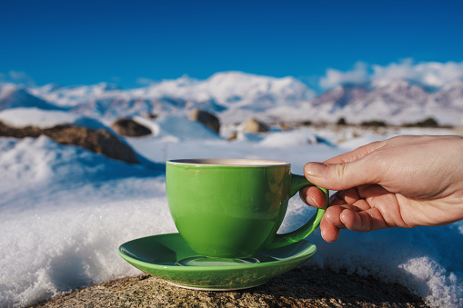 Woman holding green cup on high mountains winter background