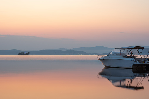 Sailing boats reflect in the serene water during sunrise. Amazing sunrise in summer morning. The silhouette is reflecting on the water. Orange and pink sky