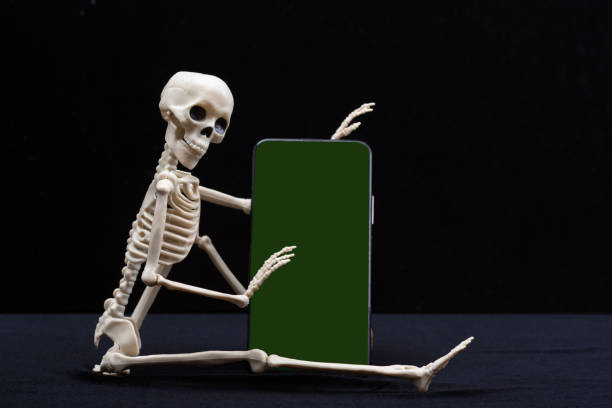 istock A seated skeleton is holding a smartphone with a green chromakey screen isolated on a black background 1509230475