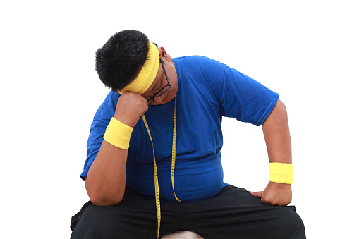 Stressed Asian overweight man in sportswear sitting against white background