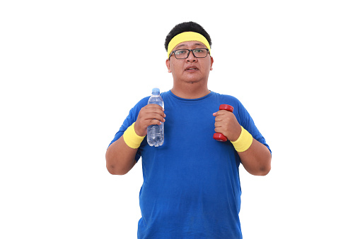 Asian overweight man in sportswear standing while holding a bottle of drink and dumbbell. Isolated