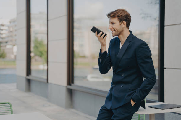 l'uomo d'affari fiducioso organizza la giornata, registra il messaggio, parla in vivavoce, appoggiato al tavolo del caffè - cafe table outdoors speaker foto e immagini stock