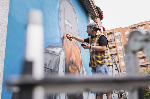 Street artist painting colorful graffiti on generic wall . Modern art concept with urban guy performing and preparing live murales.