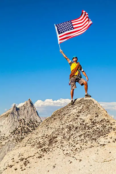 Photo of Climber waves flag on mountain peak.