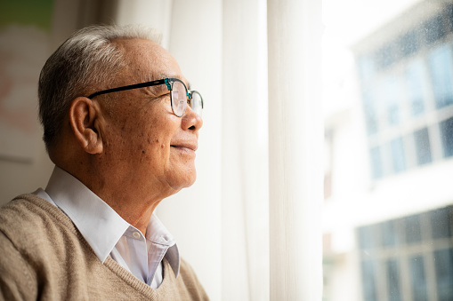Pensive elderly mature senior man in eyeglasses looking in distance out of window, thinking of personal problems.