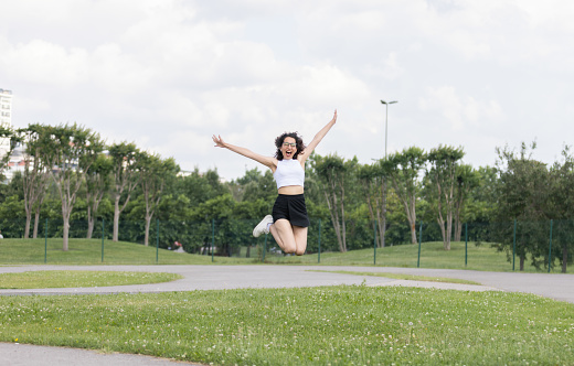 A young woman with positive vibes having fun jumping in public park.