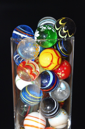 Drinking glass overflowing with colorful marbles.
