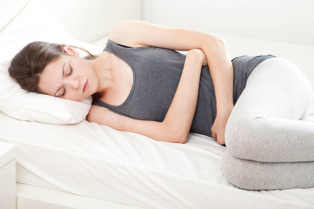 istock Woman lying down in bed clutching stomach with a grimace 150934694