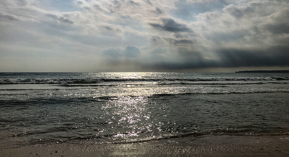 Sunlight through clouds reaches the ocean surface and the sandy beach.