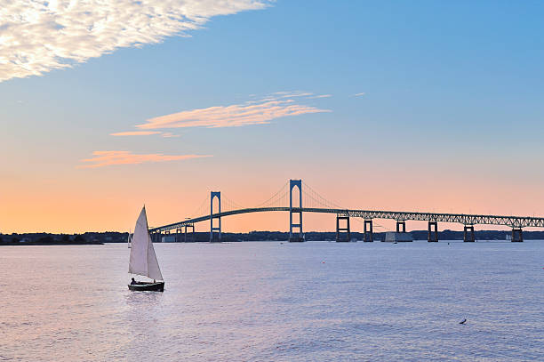 Newport Bridge Twilight Sunset with Sailboats Rhode Island USA Newport Sunset with Newport Bridge sailboats Newport, Rhode Island, USA. The person in the sailboat is in silhouette & I also changed the shape of the face, body, color of clothing, and hair. rhode island photos stock pictures, royalty-free photos & images