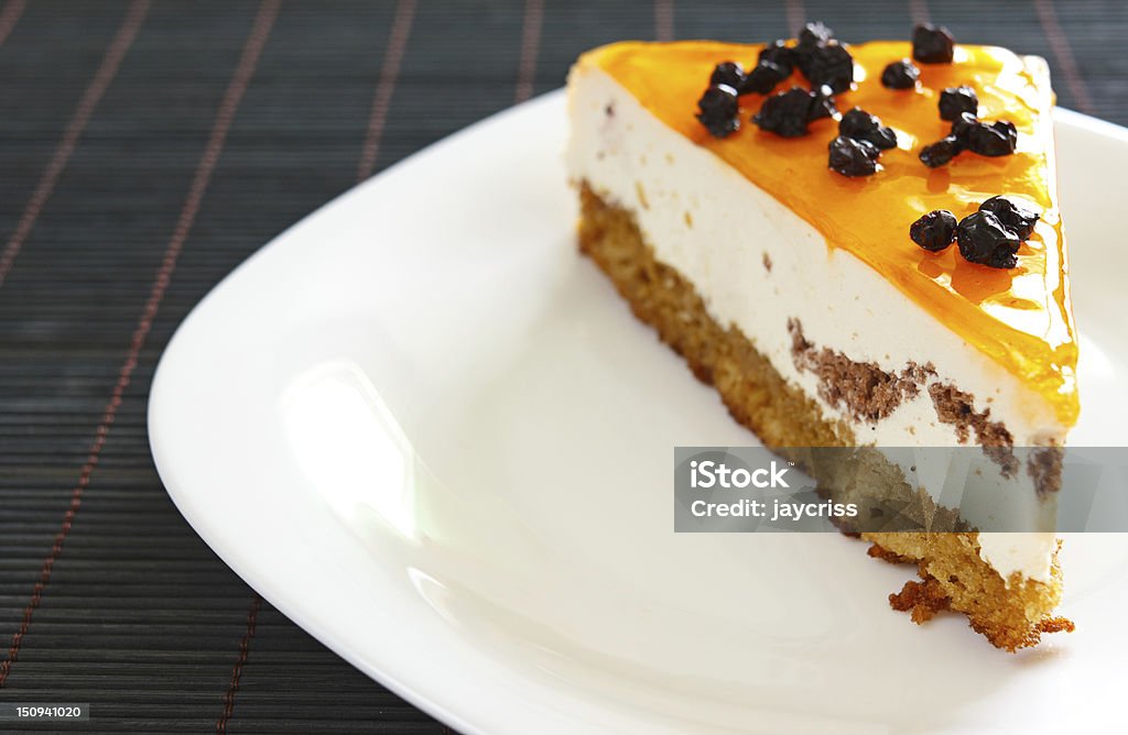 Orange jelly cake with mousse and cranberries on top Delicious orange jelly cake with mousse and cranberries on top, placed on white plate.Bamboo tablecloth.Copy space for text on the left. Cake Stock Photo