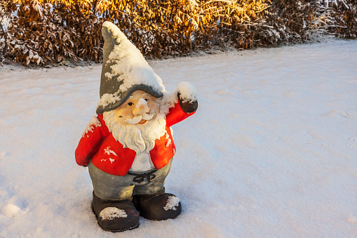 Close up view of cute figure of gnome standing in snow covered garden on sunny frosty winter day. Sweden.