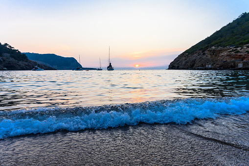 Beautiful sunset at the Benirras beach in the northwest part of Ibiza, Spain. Small waves are rolling in on the beach. The rock formation of Cap Bernat, also known as Gods Finger, can be seen in the background.