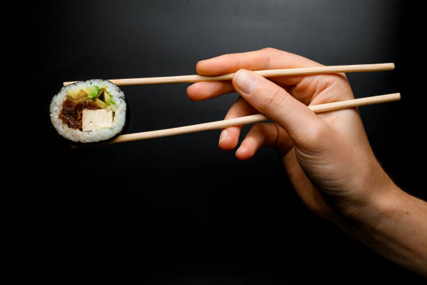 istock Woman's hand holds tasty sushi roll with smoked eel, avocado, cucumber and cheese using chopsticks 1509463595