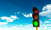 Green traffic light in front of a blue sky with clouds