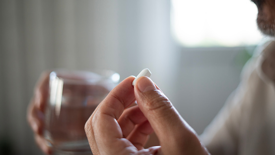 woman hand taking turmeric pill, girl hand holding turmeric powder in capsule or curcumin herb medicine with a glass of water, treatment for acid reflux problem