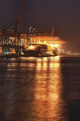 HDR of container terminal by night in the harbour of Rotterdam, The Netherlands. Motion blur in water and passing vessel.