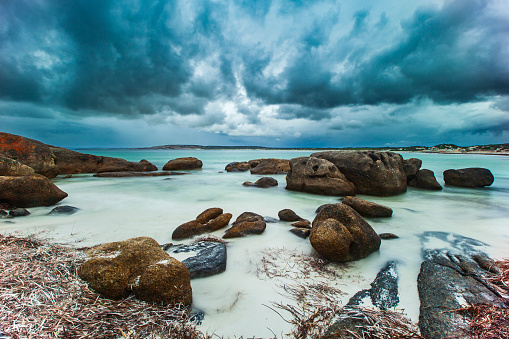 Long exposure seascape of bay of water with ominous storm clouds approaching with smooth ocean and rocky coastline in Western Australia.