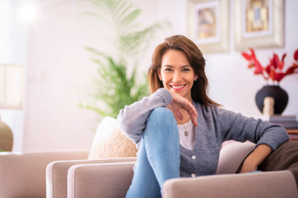 Attractive brunette haired woman wearing casual clothes and relaxing in an armchair at home stock photo