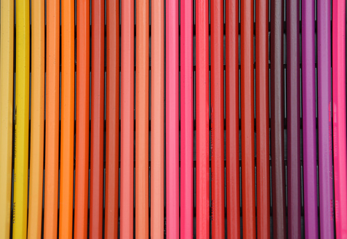 A set of Colored pencils lying in a beautiful gradient transition from yellow to pink and red, brown and purple hues. Abstract background.