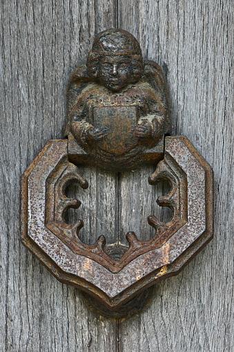 Antique door knocker with angel on weathered wooden door