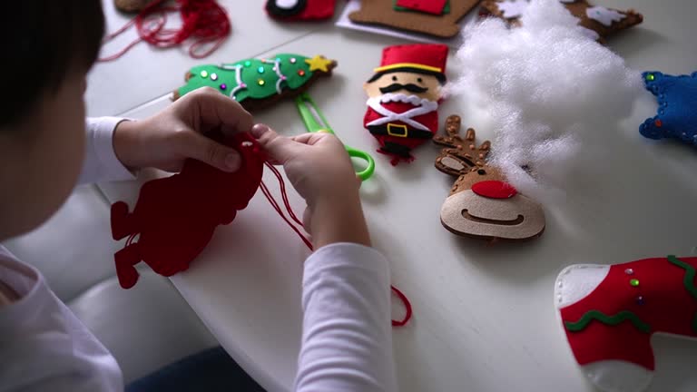 Child girl sews textile felt Santa for Christmas tree decoration. Kids festive handmade diy concept