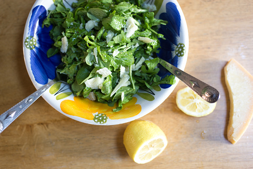 Overhead View: Arugula Salad in Bowl, Cut Lemon, Knife, Parmesan