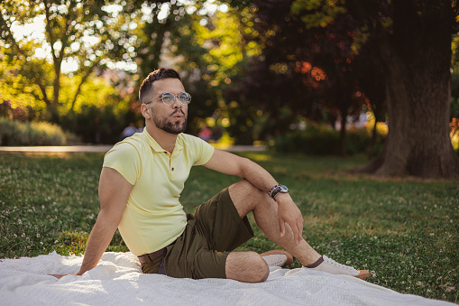 Portrait of Relaxed Whistling Man Sitting on a Blanket in the Public Park