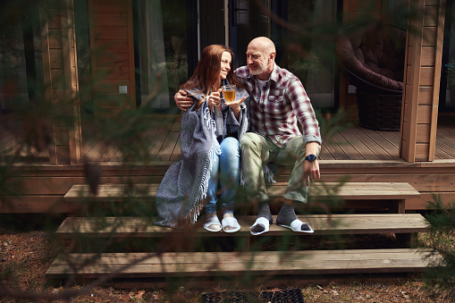 Smiling man embracing his pleased companion with cup of tea seated next to him on porch steps