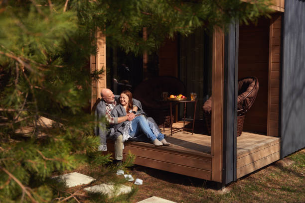 Pleased mature lady sitting on porch in arms of loving man